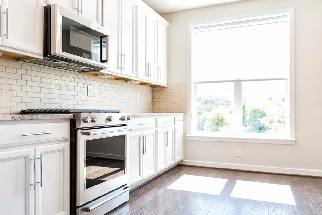 A newly renovated kitchen in an apartment complex, with hardwood floors, white cabinets, and a bright window