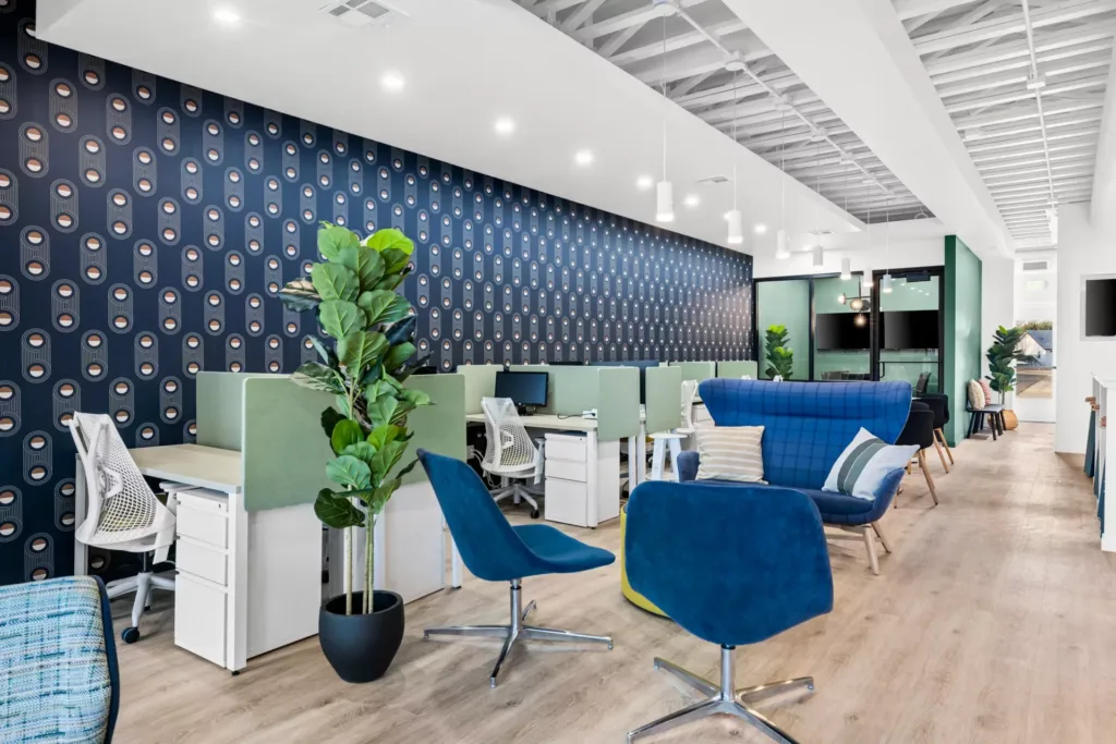 Large coworking area with blue seats and planters in a bright, well lit office space