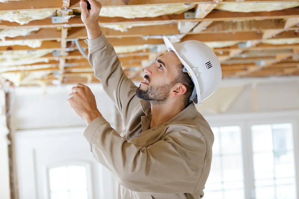 A smiling man in a hard hat, renovating the insulation inside a home