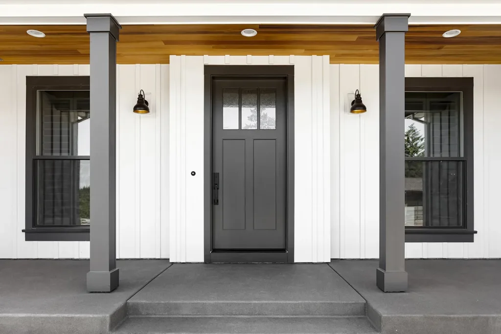 The front porch of a house with white walls and a black steel door